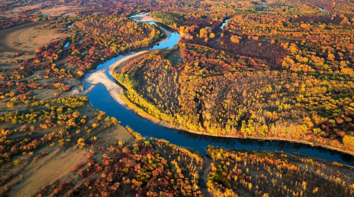 Vista aérea de un río claro rodeado de árboles otoñales, imagen decorativa para colección de moda otoño mujer